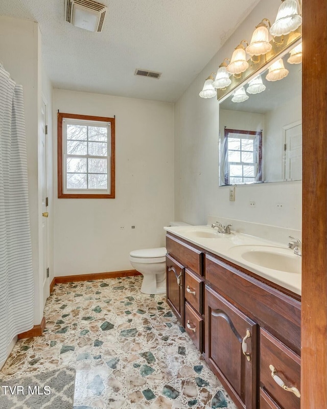 bathroom with a textured ceiling, toilet, plenty of natural light, and vanity