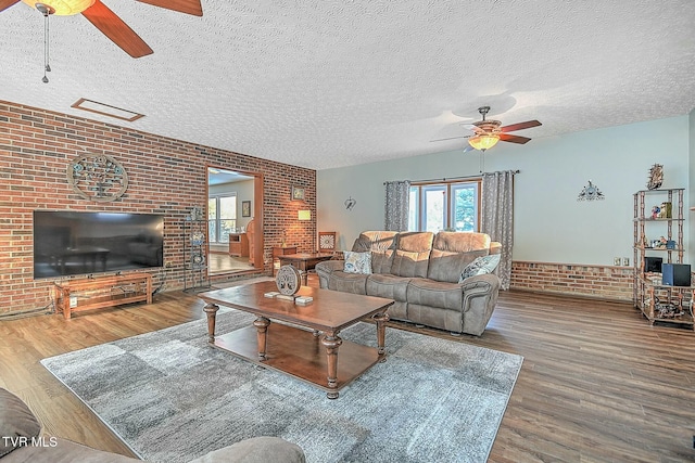 living room featuring wood-type flooring, brick wall, a textured ceiling, and ceiling fan