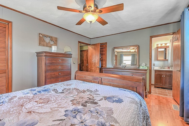 bedroom featuring ceiling fan, ensuite bath, sink, crown molding, and light wood-type flooring