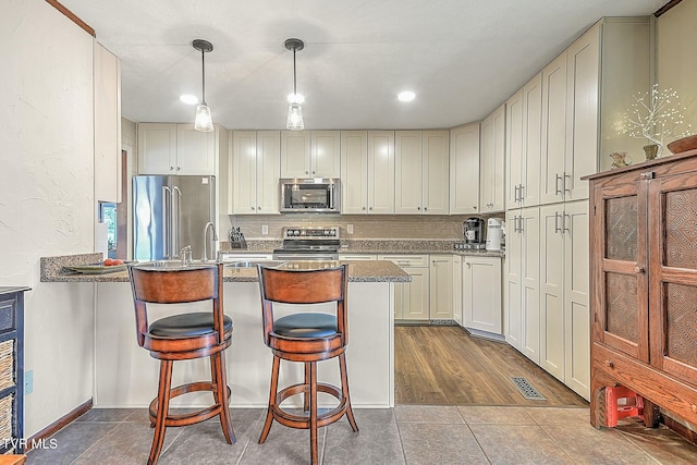 kitchen featuring appliances with stainless steel finishes, kitchen peninsula, a breakfast bar, and decorative light fixtures