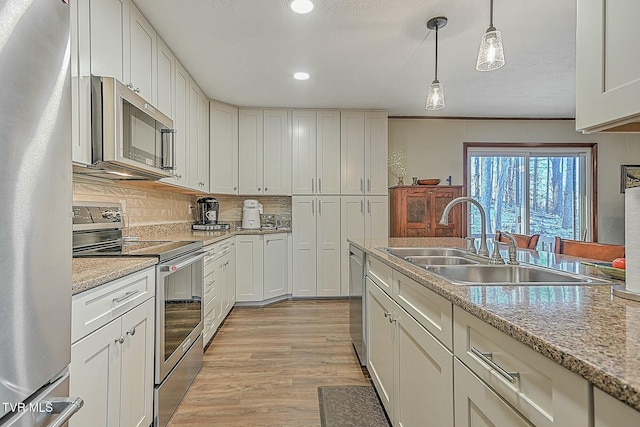 kitchen featuring decorative light fixtures, stainless steel appliances, tasteful backsplash, sink, and light stone counters