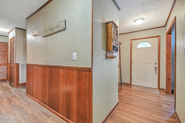 hallway with a textured ceiling, ornamental molding, and light wood-type flooring