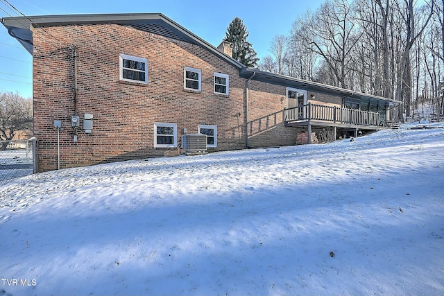 snow covered back of property featuring central AC and a deck