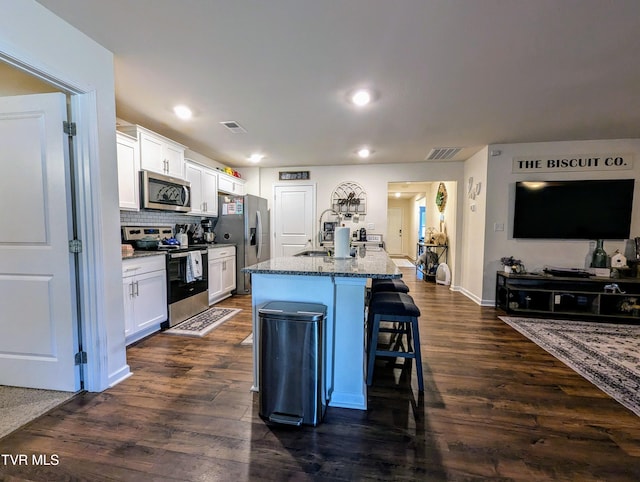 kitchen with white cabinets, stainless steel appliances, sink, a breakfast bar, and a center island with sink