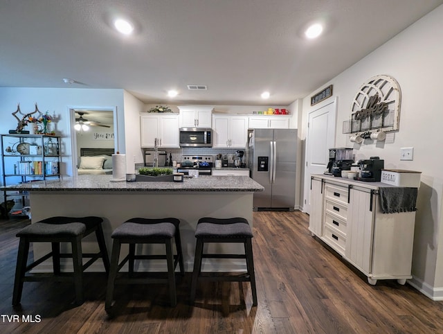 kitchen with a kitchen breakfast bar, white cabinetry, stainless steel appliances, and a kitchen island with sink