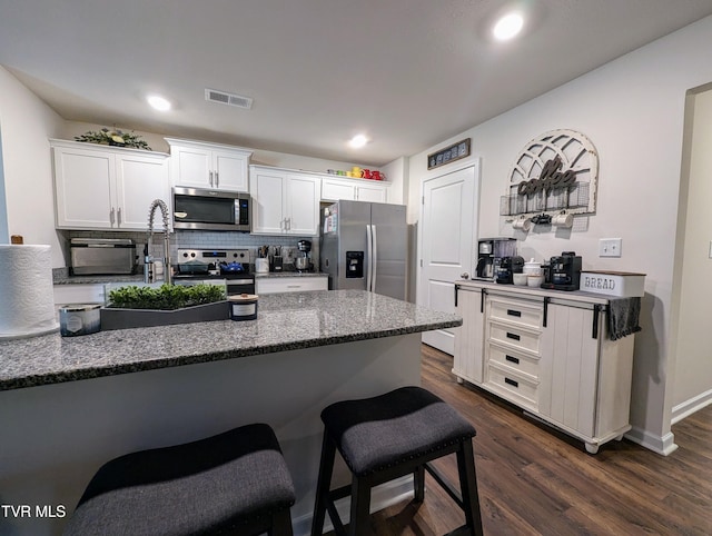 kitchen with white cabinetry, stainless steel appliances, decorative backsplash, dark hardwood / wood-style floors, and dark stone countertops