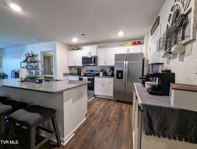 kitchen with white cabinets, appliances with stainless steel finishes, dark wood-type flooring, tasteful backsplash, and a center island with sink