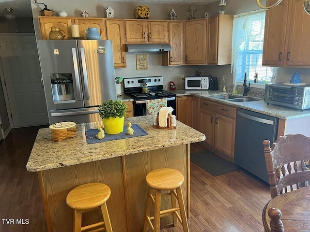 kitchen featuring appliances with stainless steel finishes, dark hardwood / wood-style floors, light stone countertops, a kitchen island, and sink