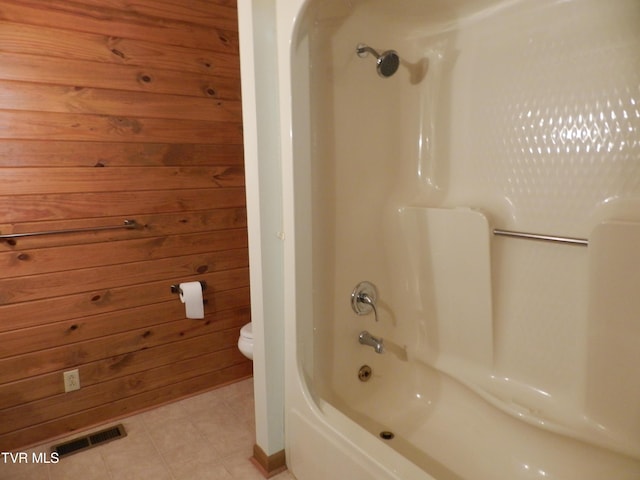 bathroom with shower / bathtub combination, wood walls, and toilet