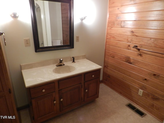 bathroom with toilet, vanity, and wood walls