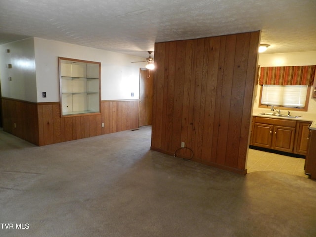 carpeted spare room with sink, wooden walls, a textured ceiling, ceiling fan, and built in shelves