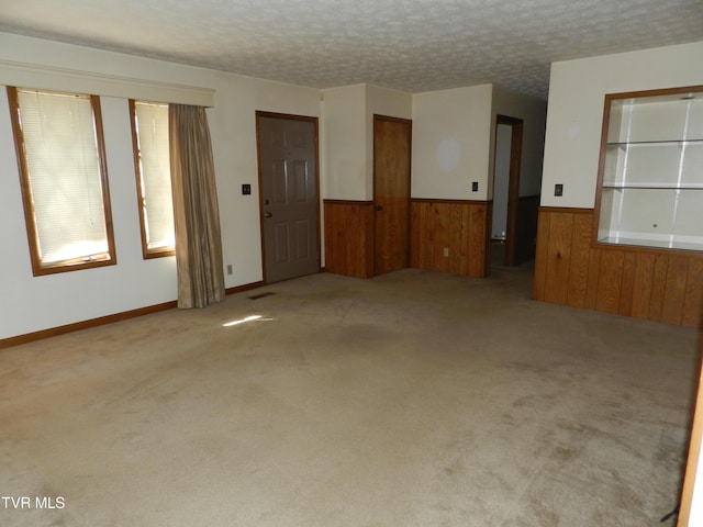 unfurnished room with wooden walls, a textured ceiling, and light carpet