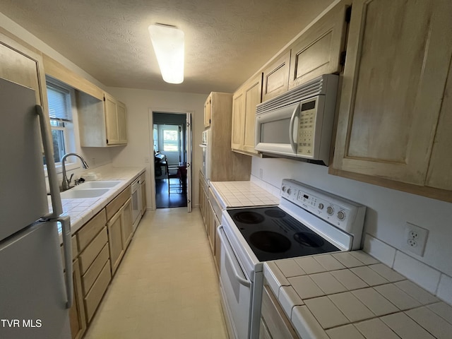 kitchen featuring white appliances, tile counters, light brown cabinetry, and sink