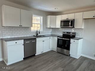 kitchen with dark wood-type flooring, stainless steel appliances, backsplash, white cabinets, and sink