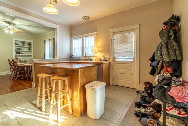 kitchen featuring a breakfast bar, ornamental molding, stainless steel dishwasher, ceiling fan, and kitchen peninsula