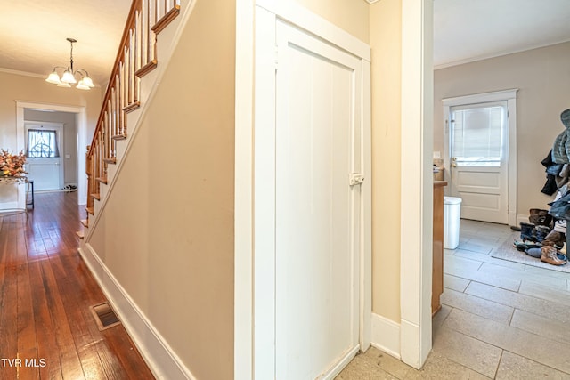 hallway with a notable chandelier, wood-type flooring, and ornamental molding