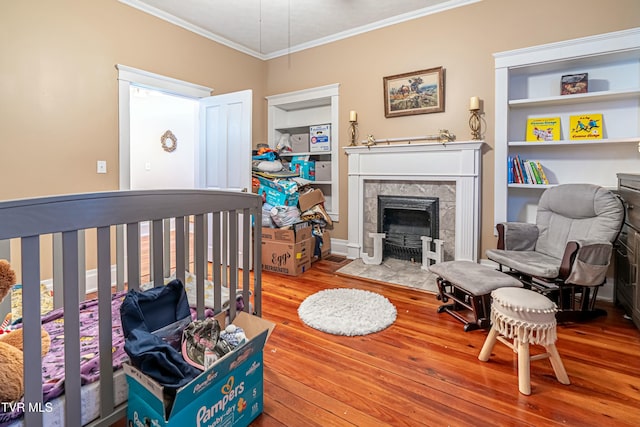 bedroom featuring a tiled fireplace, hardwood / wood-style floors, and ornamental molding