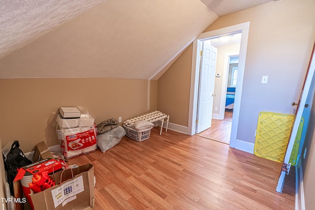 additional living space with lofted ceiling, a textured ceiling, and light hardwood / wood-style flooring