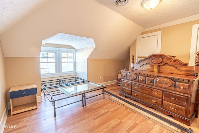 bedroom with lofted ceiling, light hardwood / wood-style flooring, and a textured ceiling