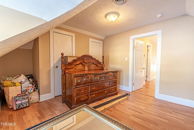 bedroom featuring vaulted ceiling, light hardwood / wood-style flooring, and a textured ceiling