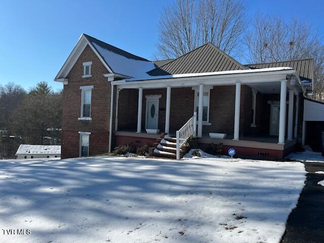 view of front facade featuring covered porch, a standing seam roof, metal roof, and brick siding