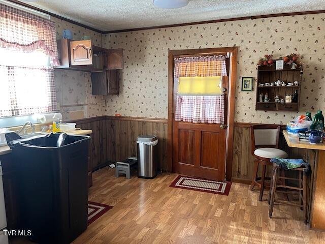 kitchen with a textured ceiling, ornamental molding, dark brown cabinets, and light hardwood / wood-style flooring