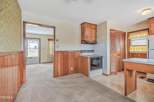 kitchen with light carpet, electric range, and wood walls