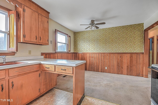 kitchen featuring sink, kitchen peninsula, wood walls, ceiling fan, and light colored carpet