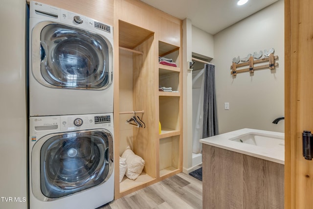 laundry area with stacked washer / drying machine, light hardwood / wood-style floors, and sink