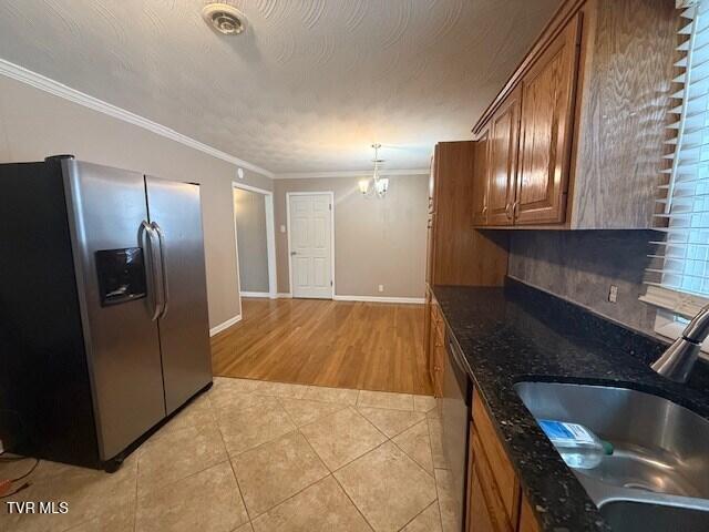 kitchen with appliances with stainless steel finishes, sink, a chandelier, light tile patterned floors, and crown molding