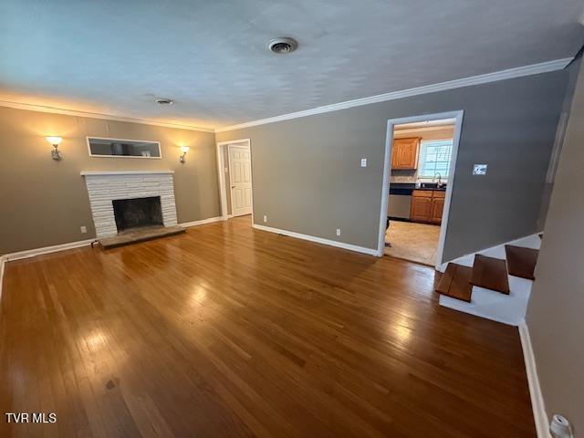 unfurnished living room with sink, dark hardwood / wood-style flooring, crown molding, and a fireplace