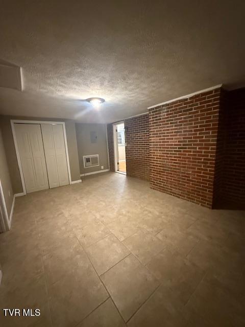 bonus room with brick wall, a textured ceiling, and a wall mounted air conditioner