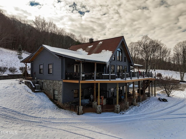 snow covered back of property with a wooden deck and cooling unit