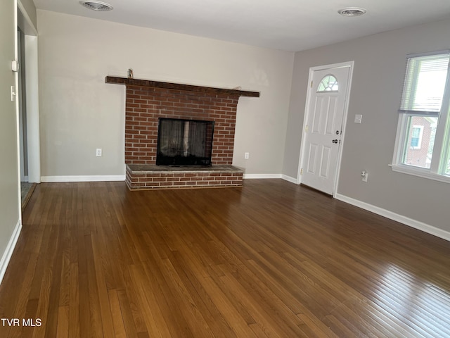 unfurnished living room featuring a brick fireplace and dark hardwood / wood-style floors