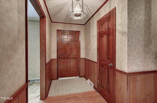 doorway with ornamental molding, light wood-type flooring, and a notable chandelier