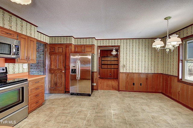 kitchen with crown molding, decorative light fixtures, a textured ceiling, a notable chandelier, and stainless steel appliances