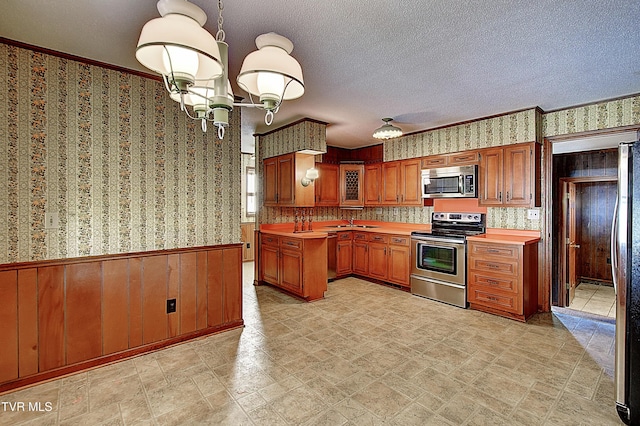 kitchen featuring pendant lighting, an inviting chandelier, stainless steel appliances, a textured ceiling, and wood walls