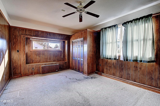 unfurnished bedroom with multiple windows, ceiling fan, radiator heating unit, and wooden walls