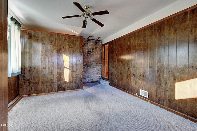 empty room featuring ceiling fan, brick wall, light carpet, and wood walls