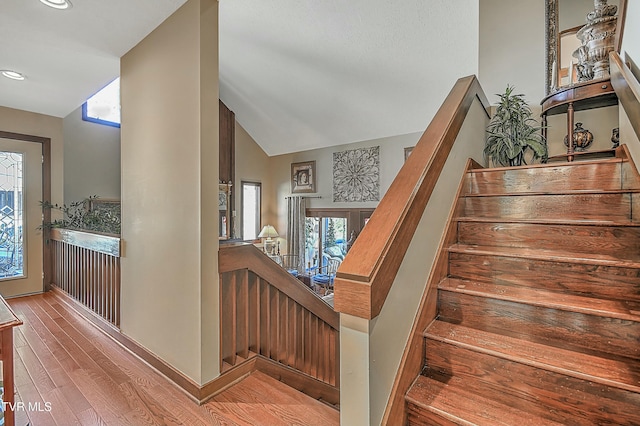 stairway with vaulted ceiling, a healthy amount of sunlight, and wood-type flooring