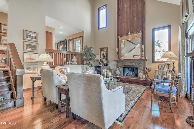 living room featuring hardwood / wood-style flooring, plenty of natural light, a towering ceiling, and a stone fireplace