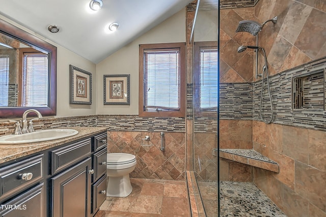 bathroom featuring toilet, tiled shower, lofted ceiling, tile walls, and vanity