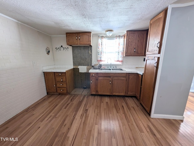 kitchen with light wood-type flooring, brick wall, a textured ceiling, and sink