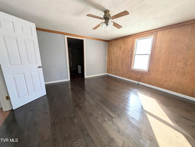 spare room featuring a textured ceiling, ceiling fan, wooden walls, and dark wood-type flooring