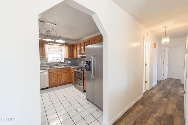 kitchen featuring a textured ceiling, stainless steel appliances, decorative backsplash, sink, and hanging light fixtures