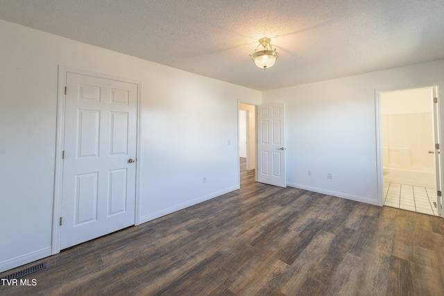 unfurnished bedroom featuring a textured ceiling, dark hardwood / wood-style floors, and ensuite bath