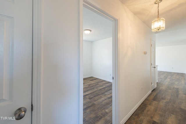 corridor with a textured ceiling, an inviting chandelier, and dark hardwood / wood-style flooring