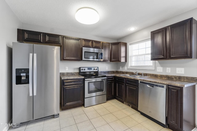 kitchen featuring sink, dark brown cabinetry, appliances with stainless steel finishes, a textured ceiling, and light tile patterned floors