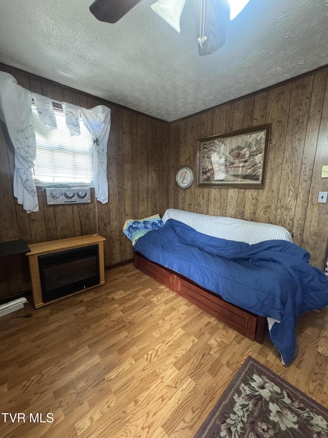 bedroom featuring a textured ceiling, wooden walls, and light hardwood / wood-style floors