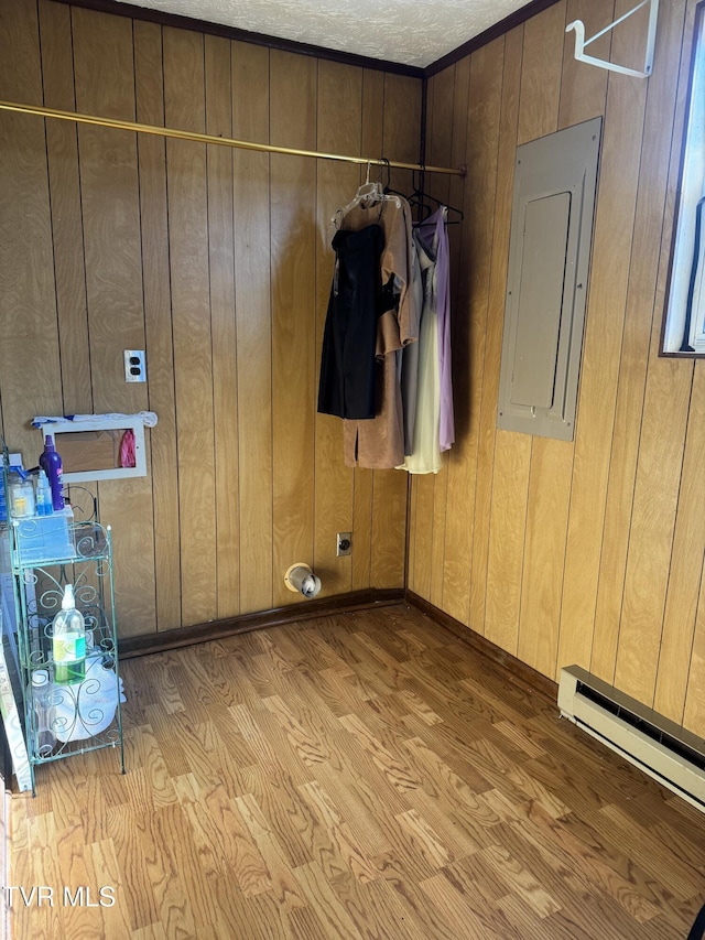 interior space with wood walls, electric panel, light hardwood / wood-style floors, baseboard heating, and a textured ceiling